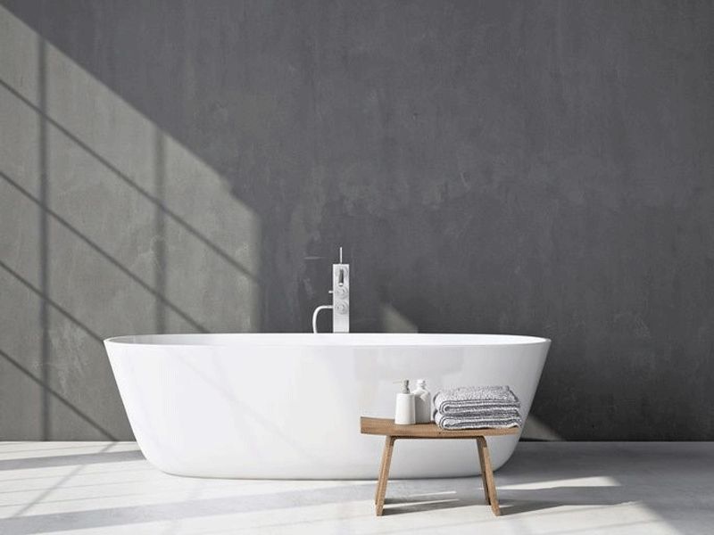 badezimmer freistehende badewanne graue betonwand holzhocker lichtschatten