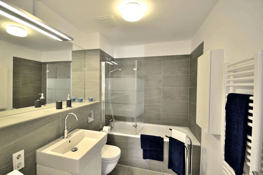 badezimmer graue fliesen badewanne glasfaltwand handtuchheizkoerper grosser spiegel